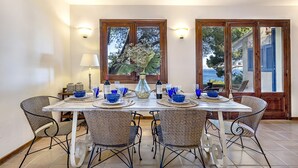 Un comedor con una mesa dispuesta para seis personas, rodeado de sillas de mimbre, y vistas al mar a través de amplios ventanales.