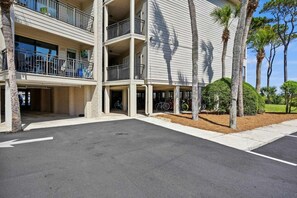 A multi-story building with balconies, a parking area, and palm trees.
