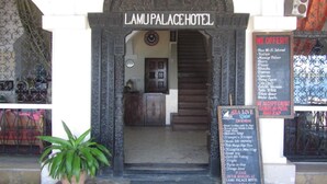 The entrance to Lamupa Palace Hotel with a sign listing amenities like free Wi-Fi, massage, and satellite TV.