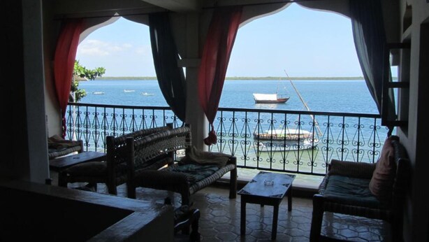 A balcony with wicker furniture, a small table, and a view of the sea with boats.