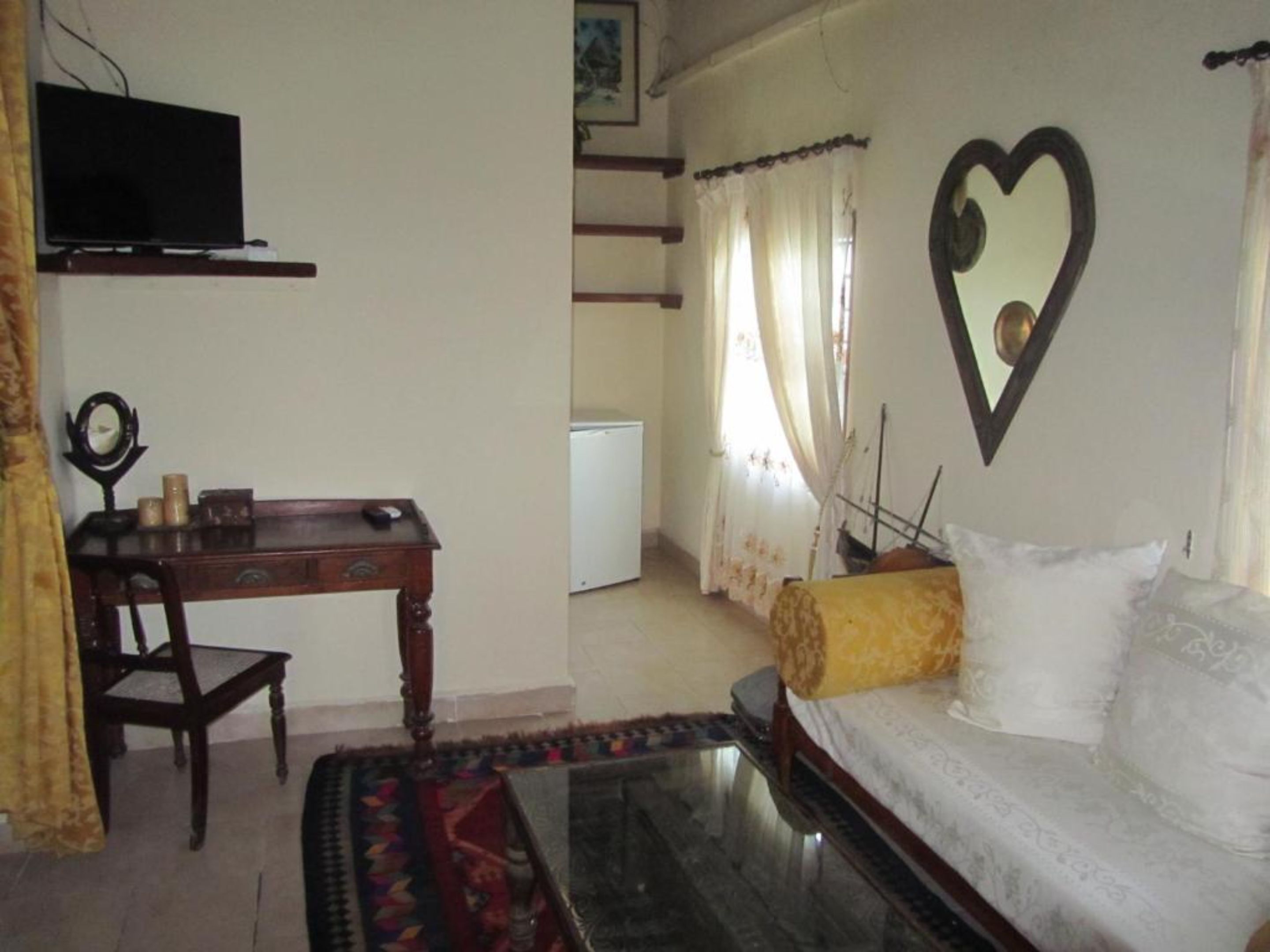 A living room with a sofa, a TV, a desk, and a heart-shaped decoration on the wall.