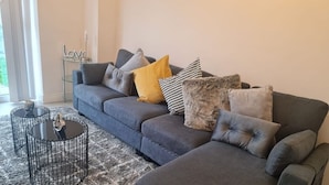 Ein modernes Wohnzimmer mit einem grauen Ecksofa, einem runden Couchtisch und verschiedenen Kissen.