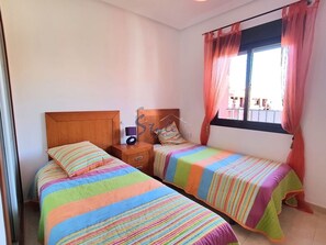 A bedroom with two beds, a wooden headboard, a nightstand, a radio, and a window with curtains. - Luxury apartment with spa, 5min. to the sea and golf course (Orihuela Costa)