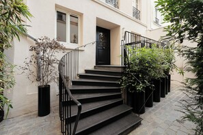 A set of black stairs leading to a black door with a decorative design, flanked by black railings and potted plants. - My Maison In Paris - Montmartre (Paris)