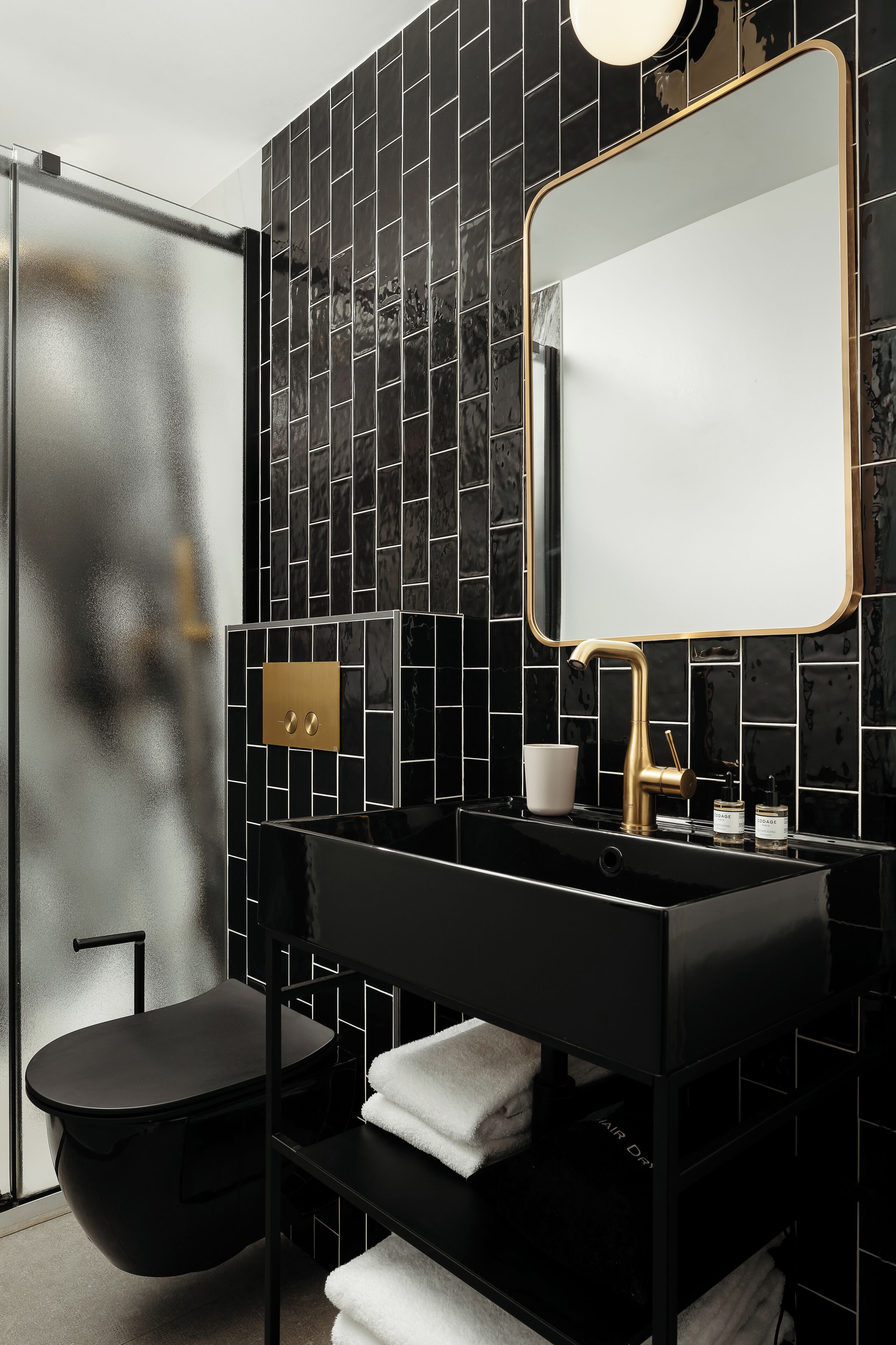 Een moderne badkamer met een zwart betegelde muur, een gouden kraan en een grote spiegel.
