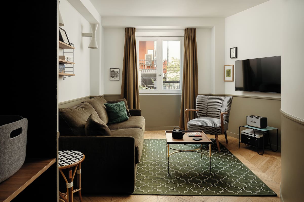 A modern living room with a sofa, armchair, coffee table, and a flat-screen TV mounted on the wall.