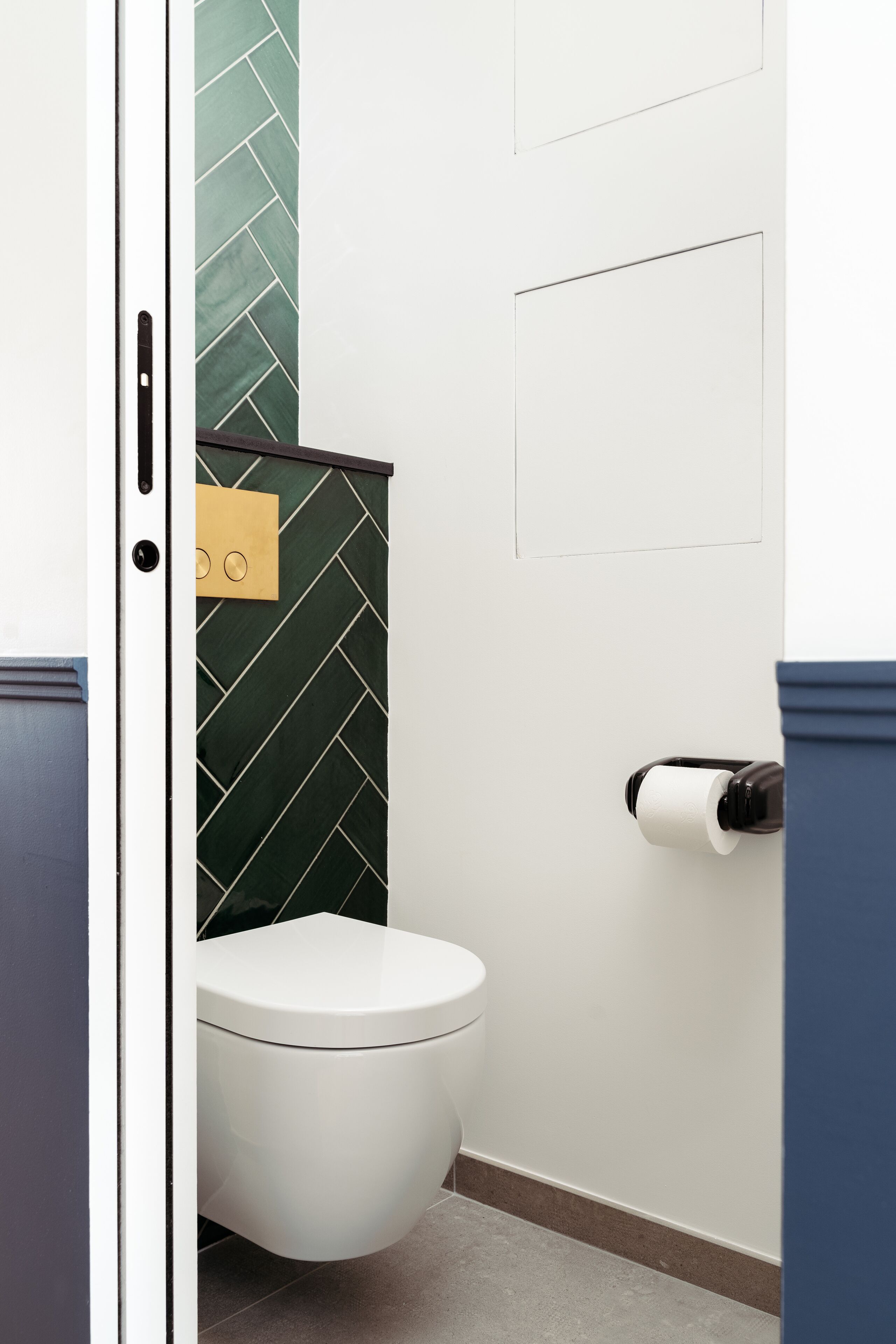 Un baño con inodoro blanco, pared con motivo de espinilla verde y un dispensador de papel higiénico.