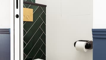 Un baño con inodoro blanco, pared con motivo de espinilla verde y un dispensador de papel higiénico.
