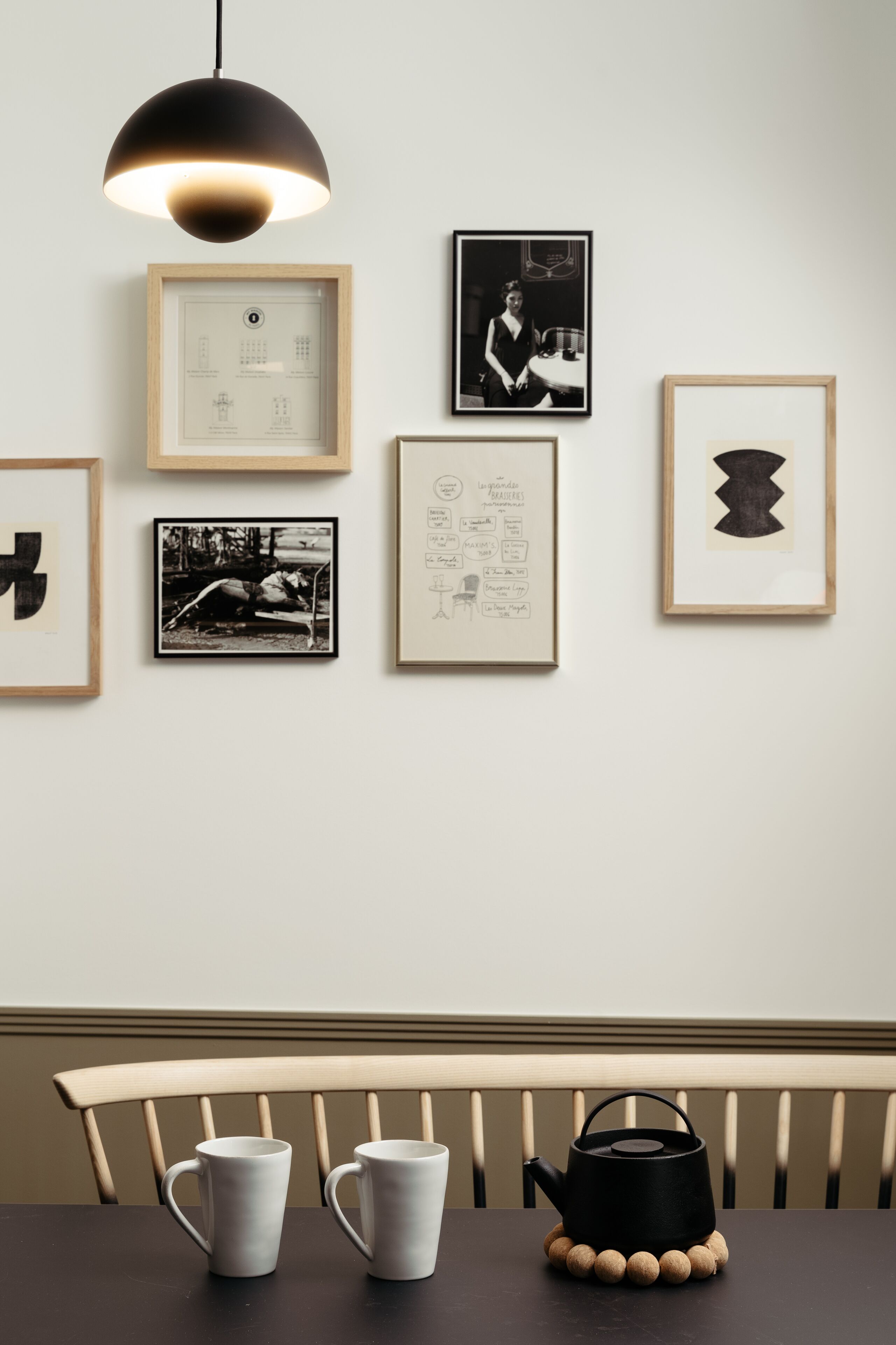 A dining area with a table, two mugs, a black teapot, and framed artwork on the wall.