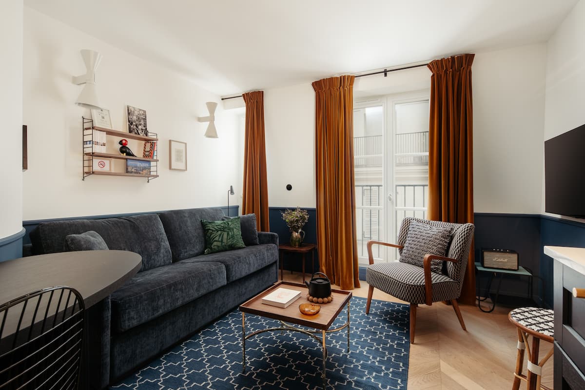 A modern living room with a dark blue sofa, a wooden coffee table, a patterned rug, a chair, and a television.