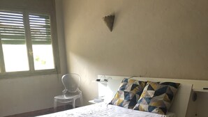 A bedroom with a bed, a chair, a bedside table, and a window with blinds. - Large F2 in private residence (Ajaccio)