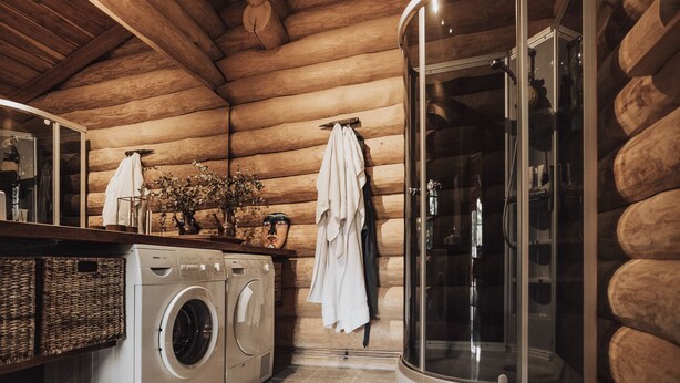 A log cabin bathroom with a washing machine, a glass shower enclosure, and wooden walls.