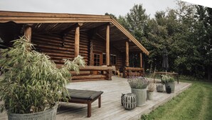A log cabin with a wooden deck, outdoor seating, and potted plants.