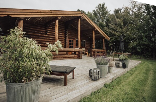 Una cabana de fusta amb terrassa de fusta, mobiliari exterior i plantes en testos.