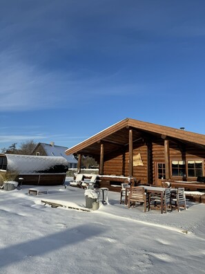 Una cabana de fusta amb un porxo cobert, mobiliari d'exterior i un terreny cobert de neu.