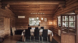A log cabin interior with a dining table, chairs, hanging light fixtures, a window, and a door.