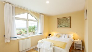 A bedroom with a large window, a bed with white bedding, a nightstand, and a radiator.