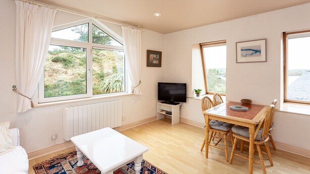 A room with a white radiator, a television on a stand, a dining table with chairs, and a window with curtains.