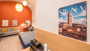 A hotel room with a wooden headboard, a bed, a desk with a lamp, a wall-mounted picture of Siena, and a red wall. - Siena Haven - Urban Suite (Budapest)