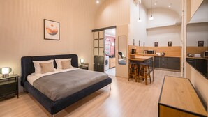 A modern hotel room with a large bed, a kitchenette, and a bathroom visible through an open door. - Siena Haven - Urban Suite (Budapest)