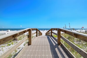 A wooden boardwalk leading to a beach with umbrellas and beachgoers.