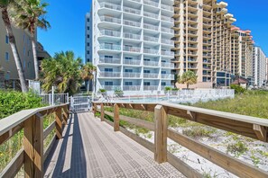 A multi-story hotel with balconies, a pool area, and a wooden boardwalk leading to the beach.