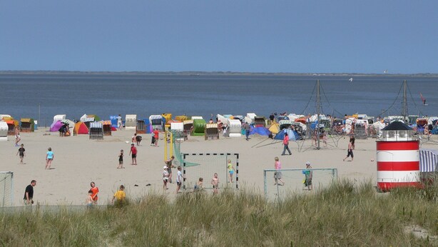 A beach with numerous colorful beach huts and a lighthouse in the foreground.