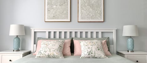 A neatly arranged bedroom with a bed, two nightstands, two wall-mounted lamps, and two framed artworks on the wall.