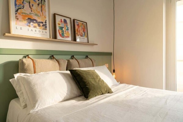 A neatly made bed with white and green pillows, a green headboard, and two framed artworks above.