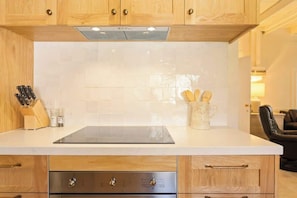 A kitchen with wooden cabinets, a white countertop, a built-in stove, and a coffee mug with utensils.