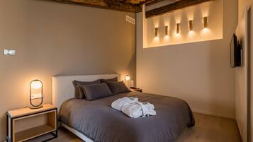 A neatly made bed with a brown bedspread, a bedside table with a lamp, and a wall-mounted light fixture.