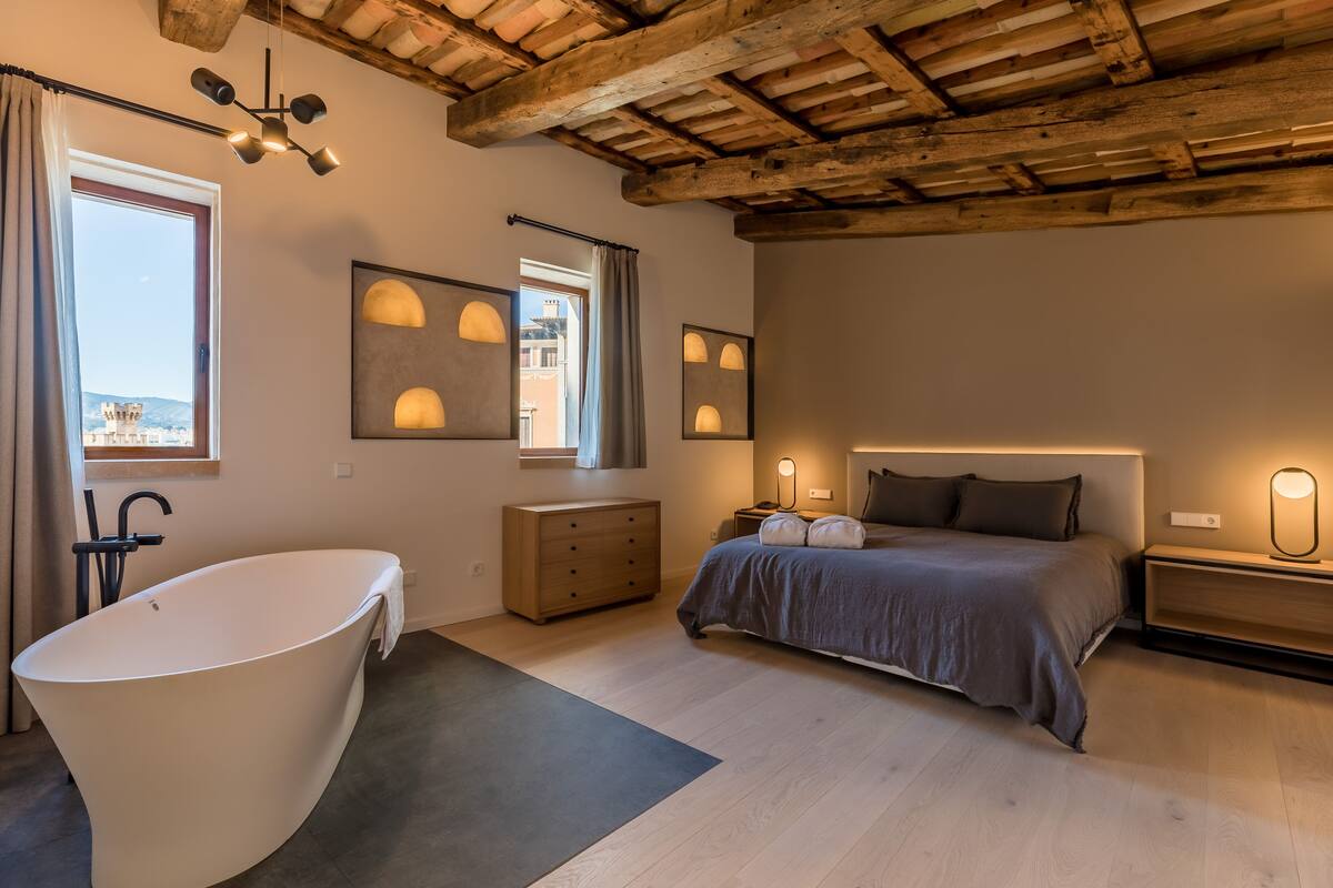 Een moderne slaapkamer met een groot bad, een bed met hoofdeinde en een houten plafond.