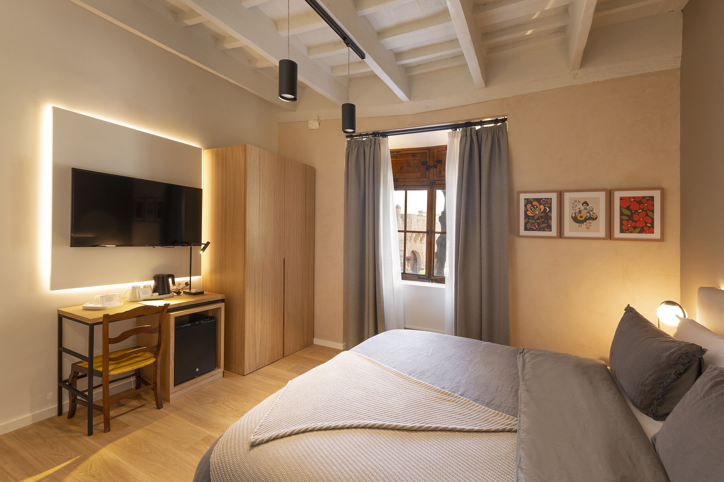 A bedroom with a bed, a desk, a television, and a window with curtains.