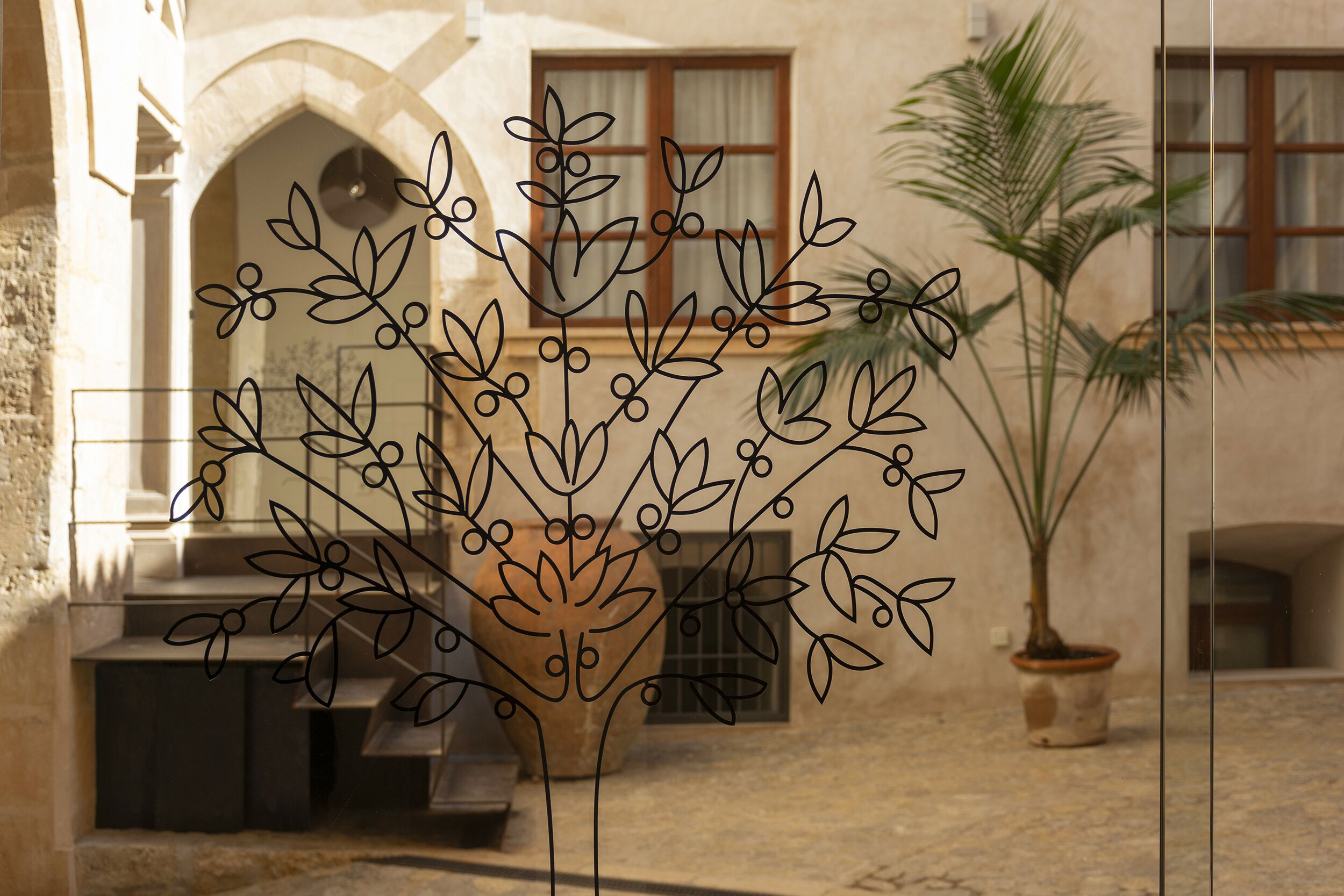 A courtyard with a stone bench, a potted plant, and a decorative metal fence with leaf patterns.