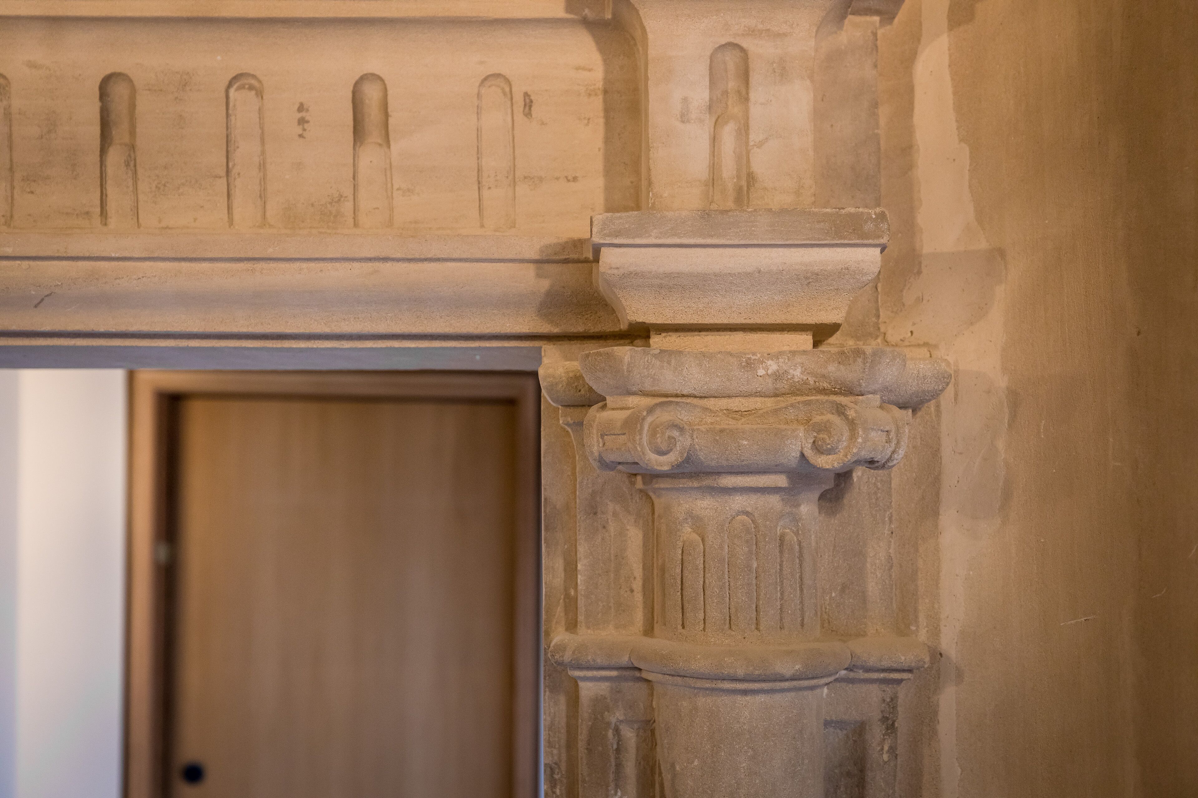 Primer plano de un detalle arquitectónico de piedra con una puerta al fondo.
