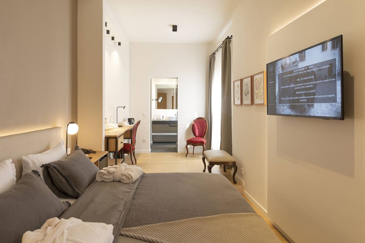 Een hotelkamer met een bed, een bureau, een stoel, een spiegel en een televisiescherm dat informatie toont.