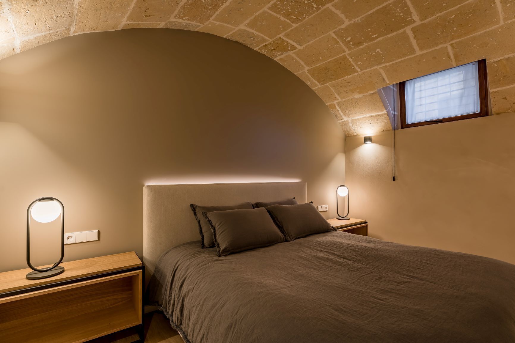 Un dormitorio con cama, lámparas de noche, mesita de noche y ventana con persianas.