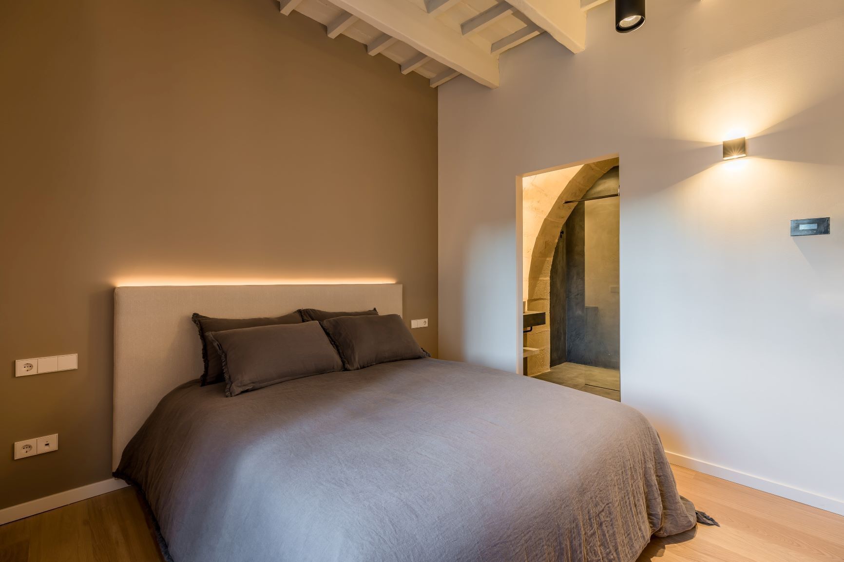 A modern bedroom with a large bed, a built-in bench, and a small alcove with a stone archway.