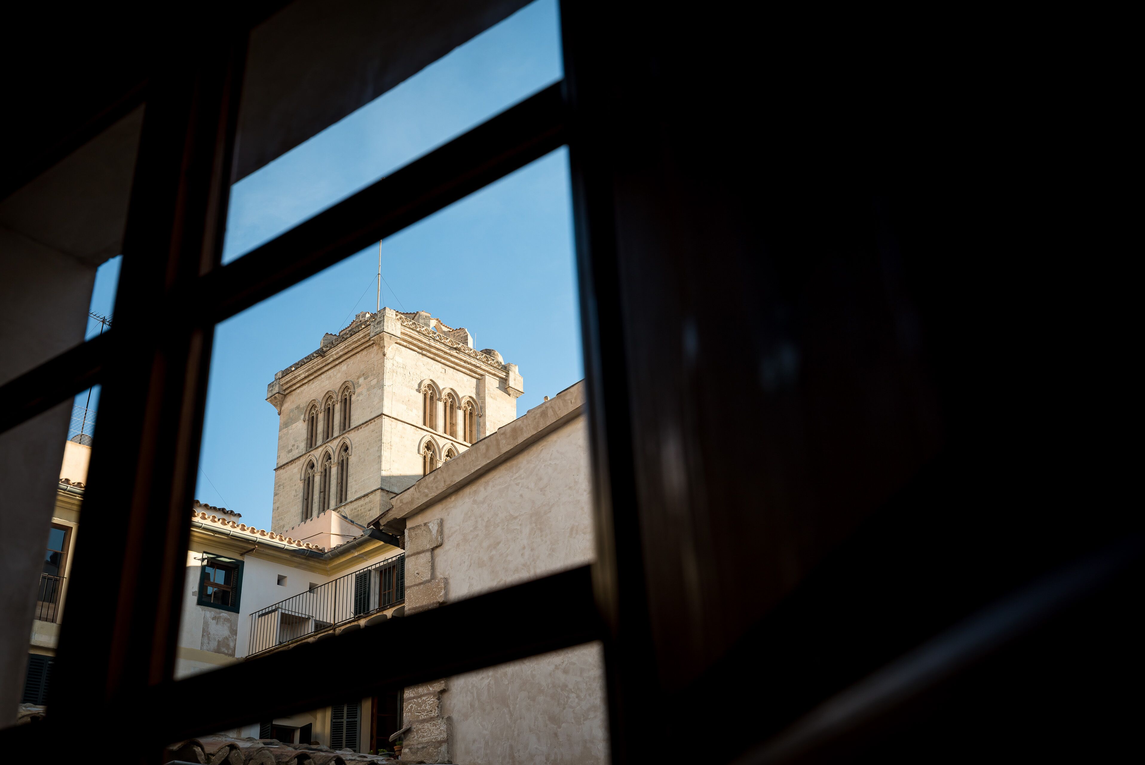 A view through a window of a building with a prominent tower and a balcony.