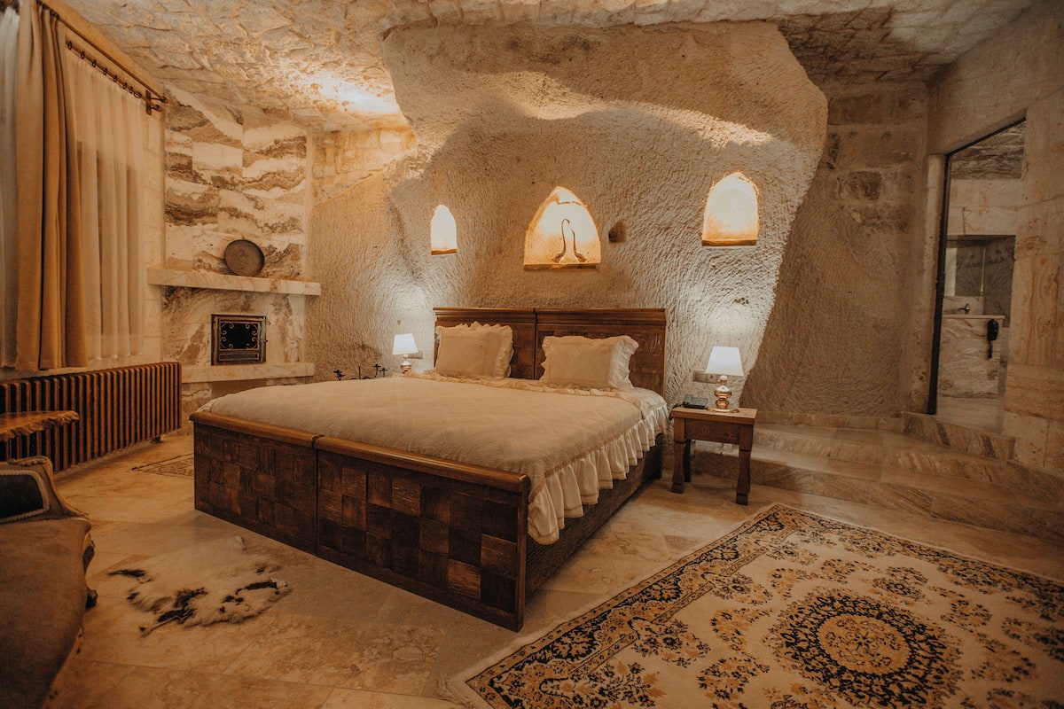 A bedroom with a stone wall, a large bed, a nightstand, and a rug.