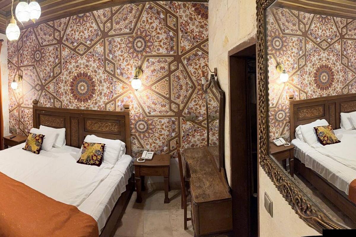 A hotel room with two beds, a wooden headboard, a desk, and a patterned wall.