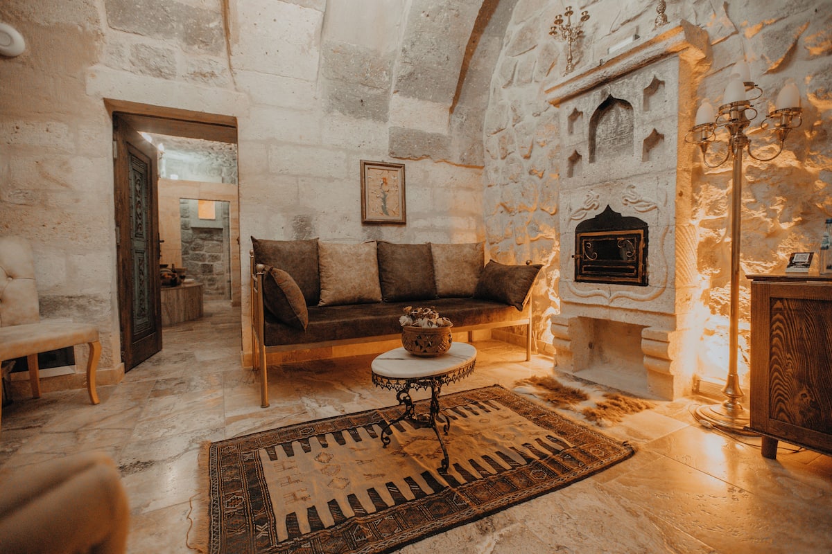 A stone-walled room with a fireplace, a sofa, a small table, and a bench.