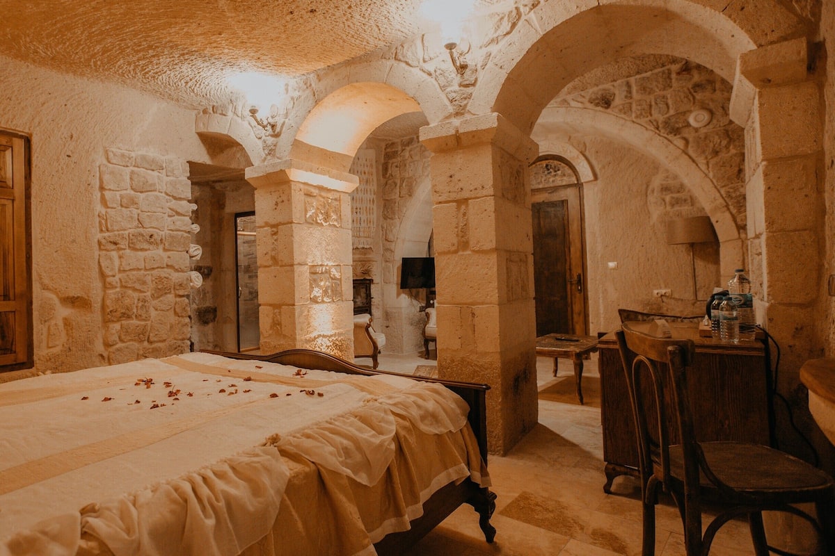 A room with a bed, wooden wardrobe, stone walls, and an arched doorway.