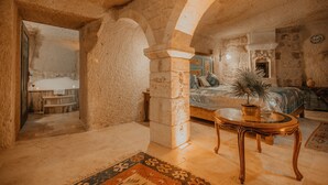 Una habitación de paredes de piedra con una cama, una mesa de vidrio y una planta en maceta.