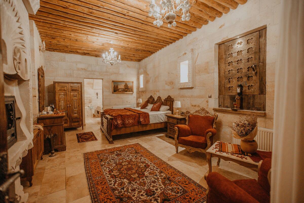 A traditional room with a wooden ceiling, a bed with a red blanket, a red armchair, and a large rug.