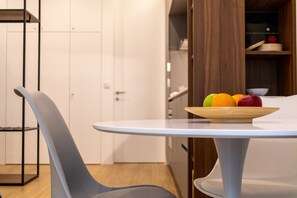 A modern kitchen with a round white table, a grey chair, and a wooden shelf with a bowl of fruit. - Studio with a terrace, 250 meters from Praia da Granja (São Félix da Marinha)
