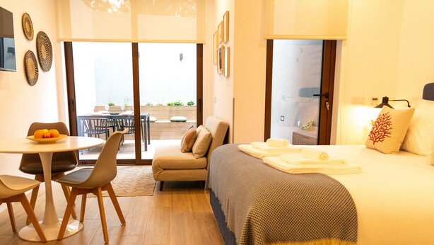 Een moderne hotelkamer met een bed, een eettafel met stoelen, een bank en een balkon met zitplaatsen buiten.