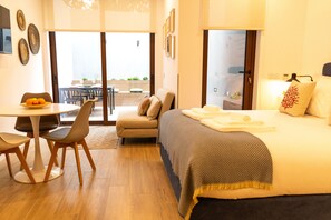 Una habitación de hotel moderna con una cama, una mesa de comedor con sillas, un sofá y un balcón con mobiliario exterior.