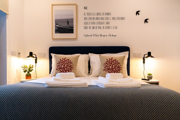 A neatly made bed with white linens and decorative pillows, a bedside table with a lamp, and a wall with a framed photo and a quote. - Studio with terrace, 250m from Praia da Granja (São Félix da Marinha)