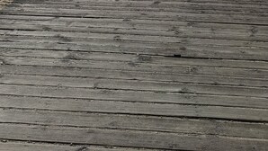 Een houten looppad leidt naar een gebouw met een rood dak, gelegen aan een strand met een bord.'